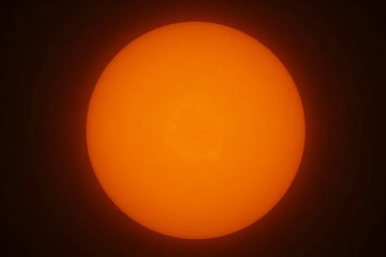 Solen syns genom ett teleskop med tydliga solfläckar mot en mörk himmel.